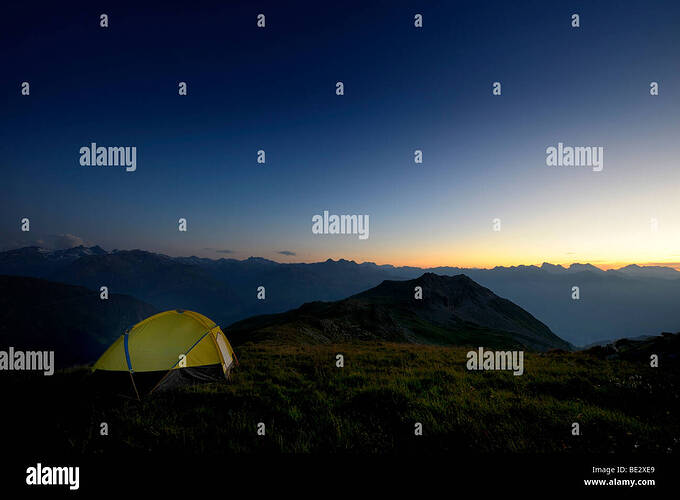 tent-in-front-of-a-mountain-range-in-the-last-daylight-gaschurn-montafon-BE2XE9